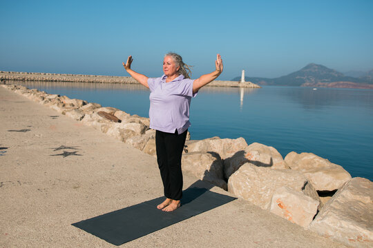 Mature woman with dreadlocks working out doing yoga exercises on sea beach - wellness well-being and active elderly age concept