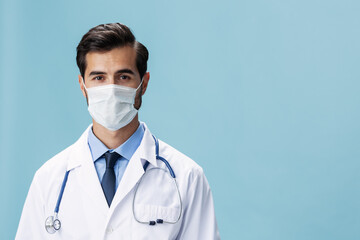 Male doctor in a white coat and medical mask looks at the camera on a blue isolated background, copy space, space for text