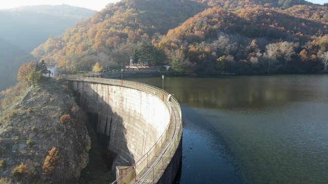 Hydropower generated from arch dam and reservoir lake with colorful autumn mountains to produce renewable energy, sustainable hydroelectricity, aerial drone view