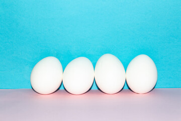 Four white chicken eggs on a blue and pink background