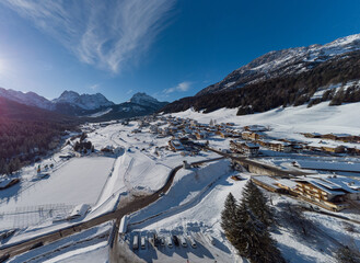 Aerial drone panorama of village of Sappada in italian Dolomites on a sunny winter day packed with snow. Beautiful alpine village in Dolomites.