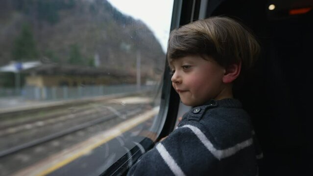 Passenger child by train window reflection. One little boy traveling looking at landscape passing by. Pensive kid