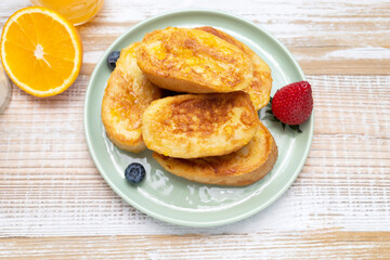 Torrijas, French Toast Made Of Sliced Brioche, Bread, Served With Orange Topping, Glaze, Fresh Blueberries, Strawberry On Green Plate, Wooden Table. A Half Of Orange. Dessert On breakfast. Horizontal