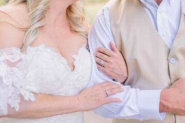 Obraz premium Bride has her arm cradling her groom's arms. She has a low cut wedding dress. 