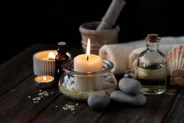 Spa setting with essential oil, candle, sea salt, pebbles, towel on dark wooden background. Massage, aromatherapy. Natural organic ingredients for relaxation, detention. Wellness in salon concept
