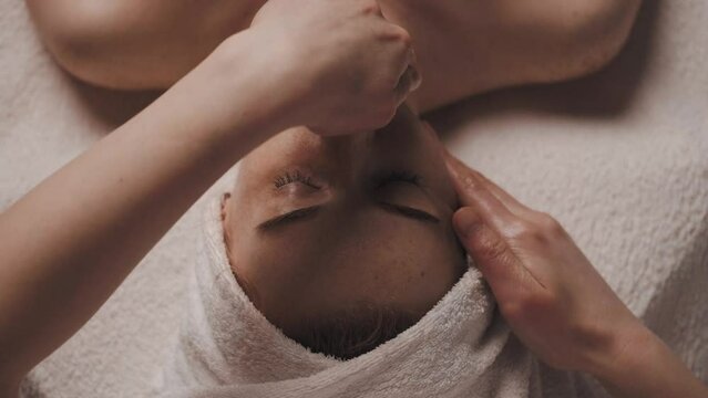 Beautiful woman with closed eyes relaxing in spa salon getting face massage in beauty spa. Serene woman relaxing in a beauty center. Professional beauty salon.