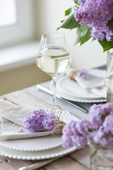 Beautiful table decor for a wedding dinner with a spring blooming lilac flowers. Celebration of a special holiday marriage event. Fancy white plates, wineglasses. Countryside style