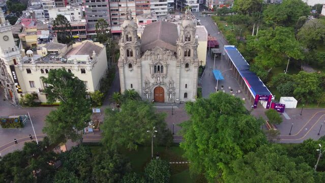 Church called "Virgen Milagrosa" surrounded by trees of park called "Parque Kennedy" Drone orbits slowly to the right. Located in Miraflores district of Lima, Peru.