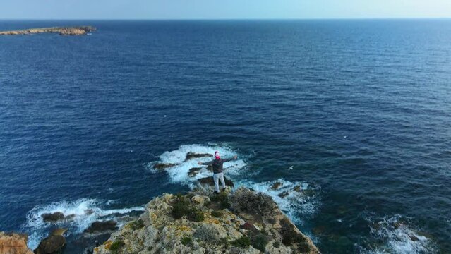 Parallax of person standing at the edge of a cliff in Spain as the drone drops below mountain.
