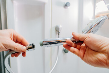 men's hands screw the shower head onto a new hose. 