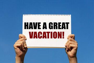 Have a great vacation text on notebook paper held by 2 hands with isolated blue sky background. This message can be used as business concept about holiday.