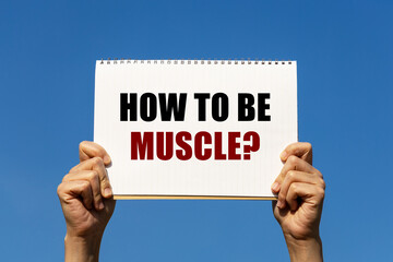 How to be muscle text on notebook paper held by 2 hands with isolated blue sky background. This message can be used as business concept about weight training.