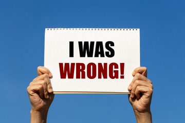 I was wrong text on notebook paper held by 2 hands with isolated blue sky background. This message...