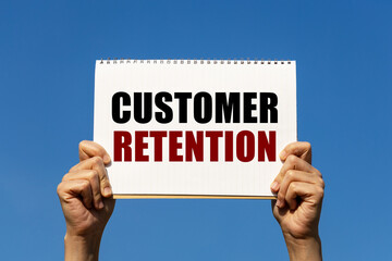 Customer retention text on notebook paper held by 2 hands with isolated blue sky background. This message can be used as business concept about customer retention.