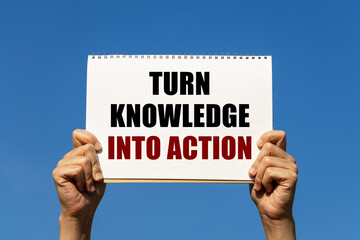 Turn knowledge into action text on notebook paper held by 2 hands with isolated blue sky background. This message can be used as business concept about turning knowledge into action.