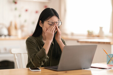 Tired korean woman digital nomad rubbing eyes, using laptop