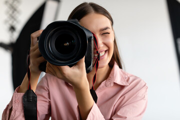 Happy young woman photographer with photocamera in her hands working in photostudio with lighting equipment