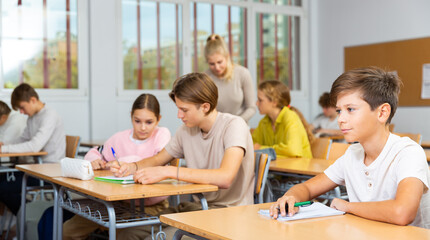 Teenagers sitting at desks in classroom during lesson and doing tasks.