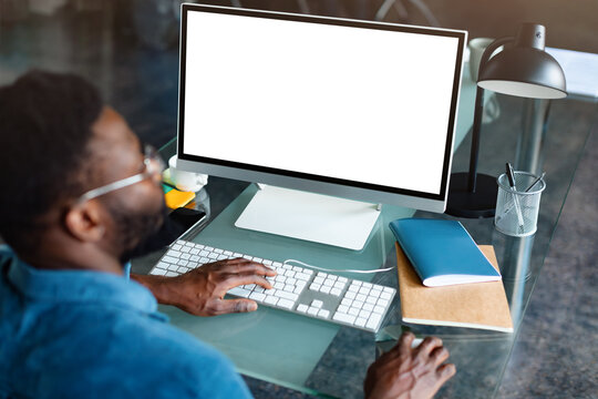 Unrecognizable black businessman using computer with empty blank screen, offering space for mockup on monitor