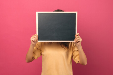 Young woman is holding and hiding her face behind a small blank black board.