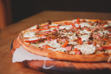Detail view of a bacon and ham pizza on a wooden table.
