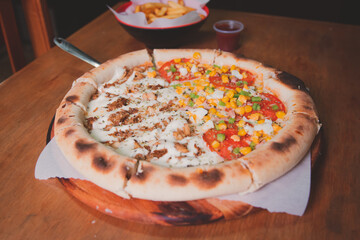 Pizza with vegetables, chicken in small pieces and lots of cheese on a wooden table.