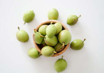 A bowl of fresh unripe peaches on a white background. Fresh raw green peach in wooden bowl. top view.