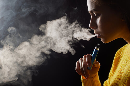young girl smokes a vape close-up on a dark background