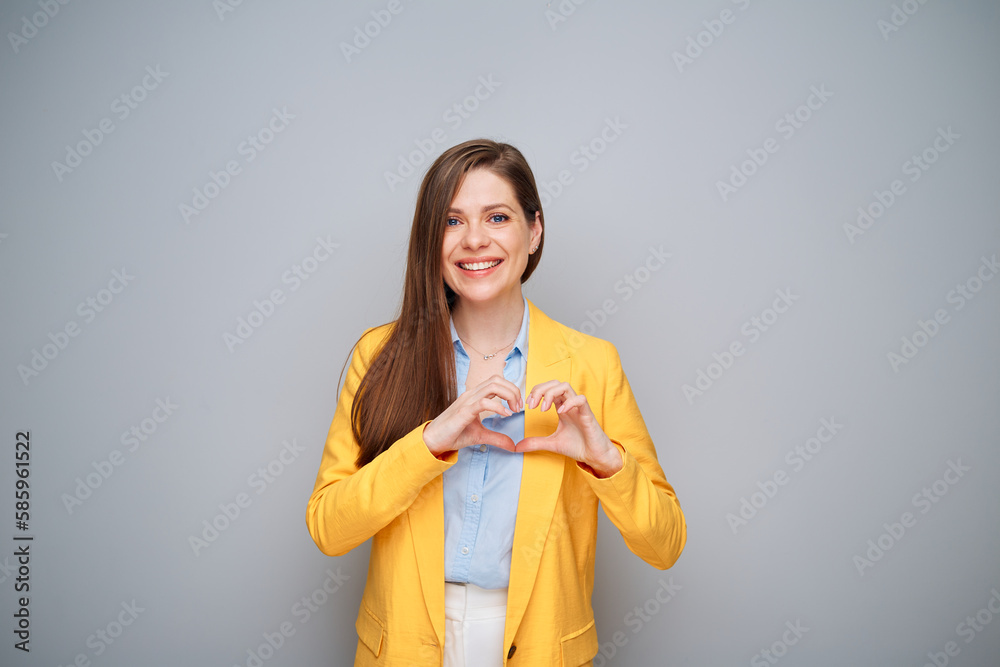 Poster Smiling woman in yellow jacket doing heart shape with fingers on gray background