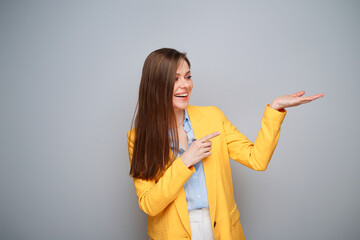 Happy smiling woman in yellow jacket pointing finger at empty hand.