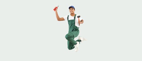Fototapeta na wymiar Jumping African-American young man in uniform and with tools on light background