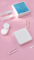 lenses, a container for lenses, tweezers and a small mirror lie on a pink background. contact lens tools