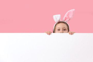 Little girl in bunny ears with blank poster on pink background. Easter celebration