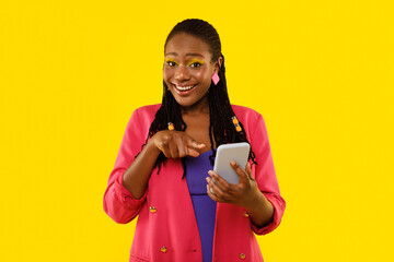 Happy Black Female Pointing At Cellphone Smiling Over Yellow Background