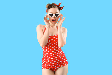 Shocked young pin-up woman in polka dot swimsuit on blue background