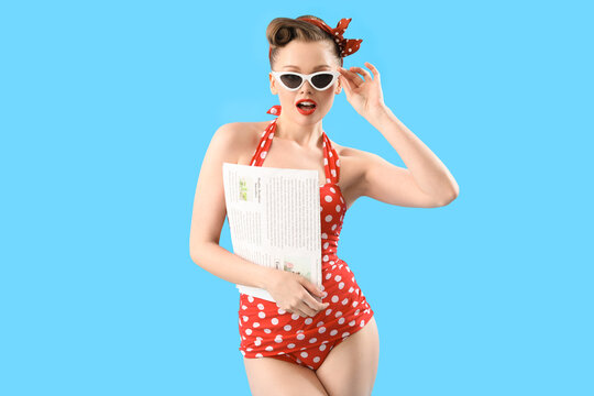 Young pin-up woman in swimsuit with newspaper on blue background
