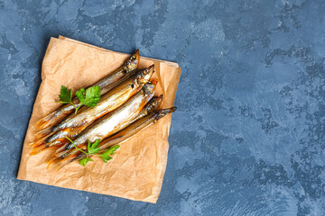 Parchment with delicious smoked capelin on blue grunge background