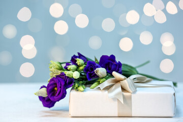 Gift and beautiful eustoma flowers for Mother's Day celebration on table against blurred lights
