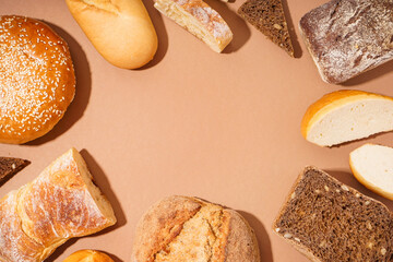 Frame made of fresh loaves of different bread on brown background