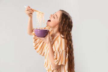 Young woman eating Chinese noodles on light background