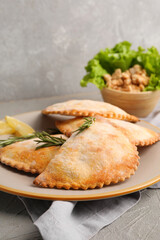 Plate with baked meat empanadas and rosemary on grunge background, closeup
