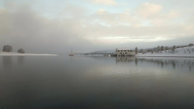 Drone flying low over fjord of Kvaloya or Sallir island in Tromso Municipality on winter and snowy day, Norway. Aerial forward