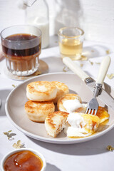 Plate of tasty cottage cheese pancakes with sour cream, jam and coffee on light table, closeup
