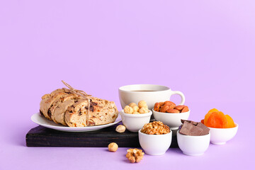 Board with biscotti cookies, chocolate, nuts, dried apricots and cup of coffee on lilac background
