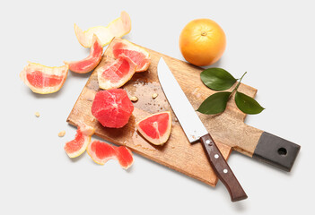 Wooden board with ripe grapefruits, peel and knife on white background