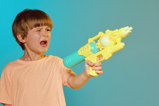 Smiling kid boy 6 years old wearing t-shirt polo hold in hand toy water gun on turquoise background