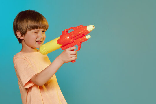 Smiling kid boy 6 years old wearing t-shirt polo hold in hand toy water gun on turquoise background