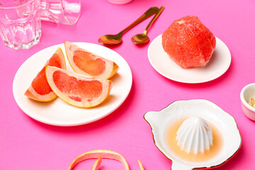 Plates with ripe grapefruits and juicer on pink background