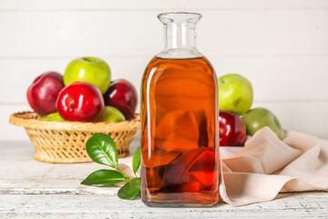 Glass bottle of fresh apple cider vinegar and basket with fruits on white wooden table