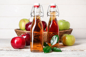 Glass bottles of fresh apple cider vinegar and basket with fruits on white wooden table